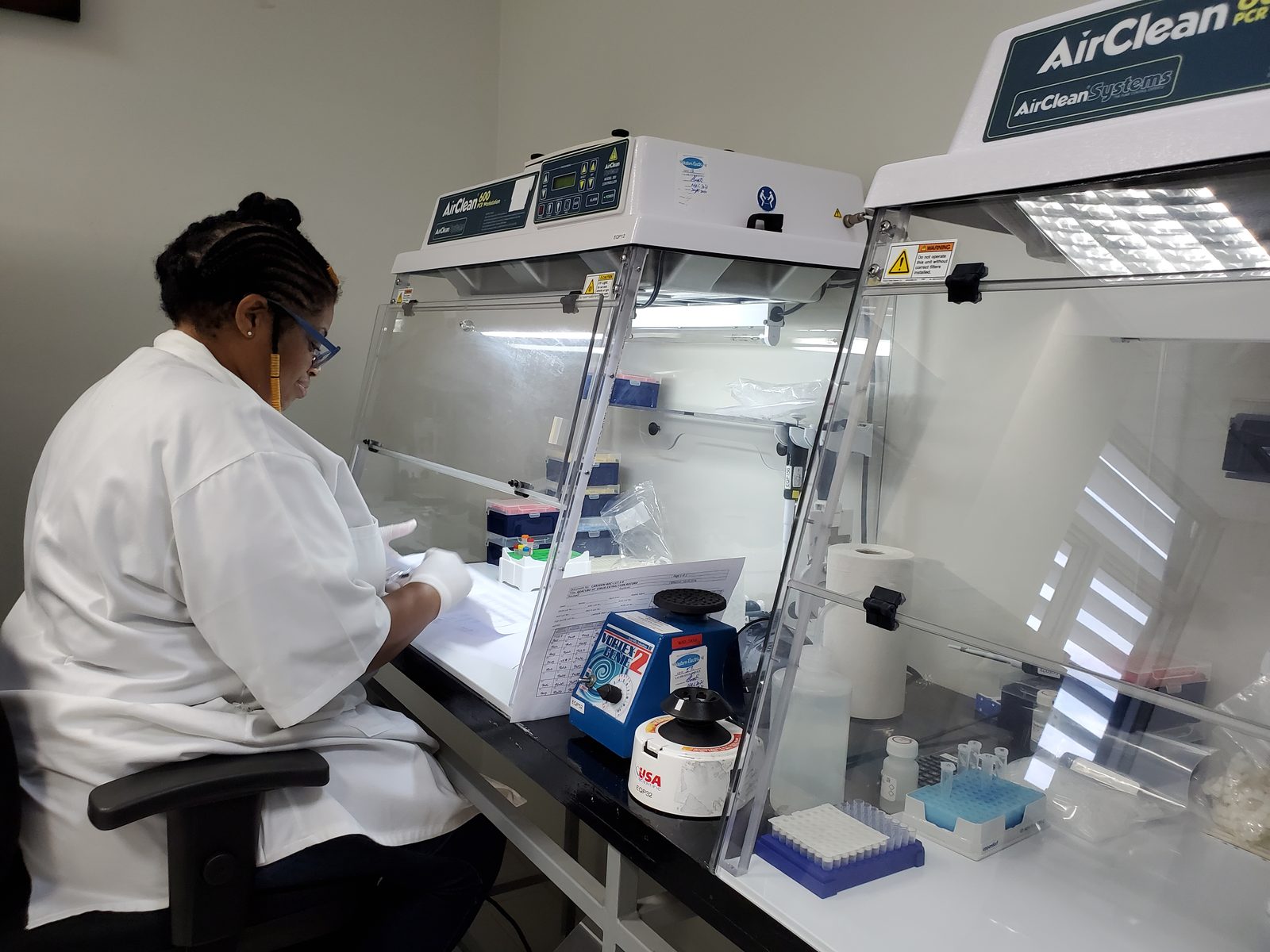 A CARIGEN analyst in a lab coat preparing samples at a laminar-flow workstation